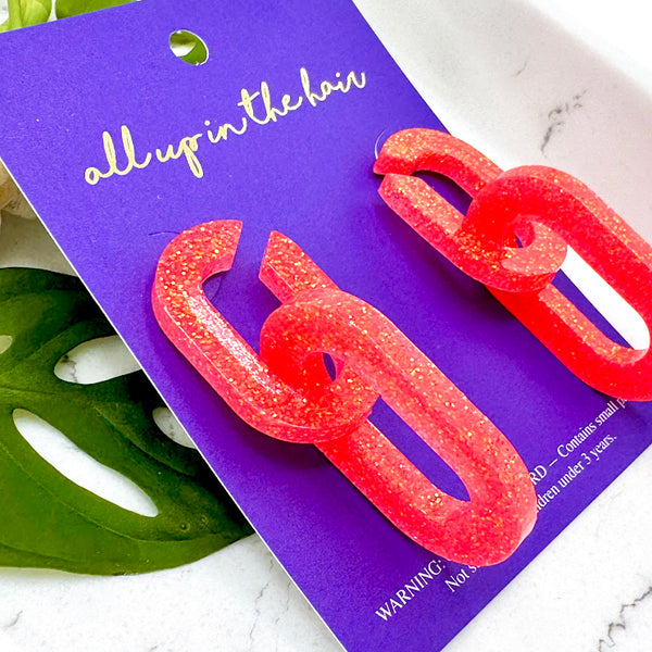 All Up In The Hair | Online Accessory Boutique Located in Mooresville, NC | Side view of two Coral Chunky Chain Earrings on an indigo backer card. The card is laying on monstera leaves on a white background.