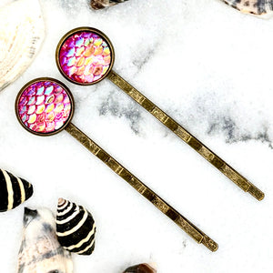 All Up In The Hair | Online Accessory Boutique Located in Mooresville, NC | Two Pink Mermaid Bobby Pins laying on a white marble background surrounded by shells.