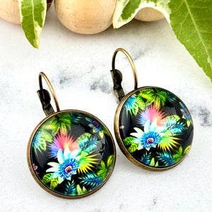 All Up In The Hair | Online Accessory Boutique Located in Mooresville, NC | Two Tropical Flower Dangle Earrings on a white marble background. There is a wood bead garland and ivy leaves behind the earrings.