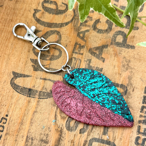 All Up In The Hair | Online Accessory Boutique Located in Mooresville, NC | A red and green half moon alocasia leaf key chain on a wood background with black lettering.