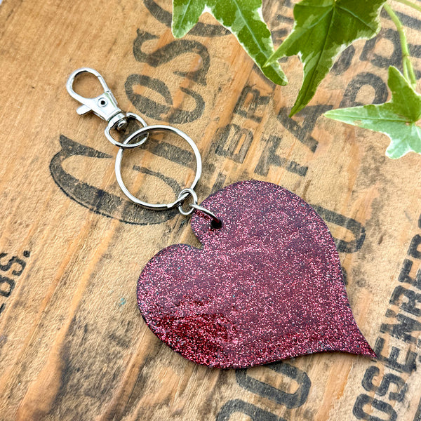 All Up In The Hair | Online Accessory Boutique Located in Mooresville, NC | Red glitter back of our Anthurium Leaf Keychain on a wood background with black lettering.