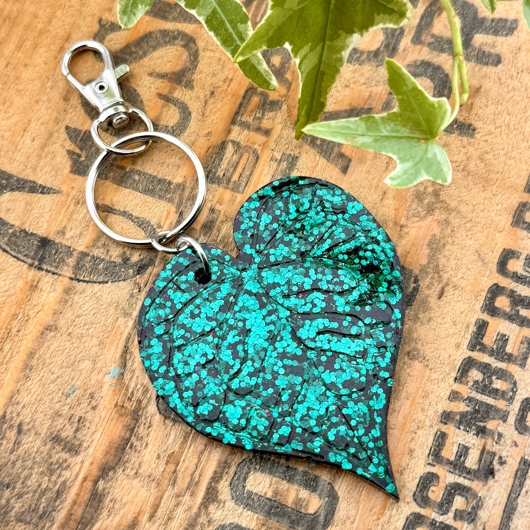 All Up In The Hair | Online Accessory Boutique Located in Mooresville, NC | Green Glitter Anthurium Leaf Keychain on a wood background with black lettering.