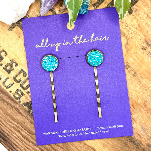 All Up In The Hair | Online Accessory Boutique Located in Mooresville, NC | Two Aquamarine Druzy Bobby Pins on an indigo colored, All Up In The Hair branded packaging card. There are crystals and ivy leaves at the top of the image.