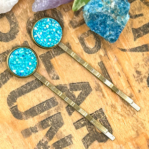All Up In The Hair | Online Accessory Boutique Located in Mooresville, NC | Two Aquamarine Druzy Bobby Pins laying on a book page.