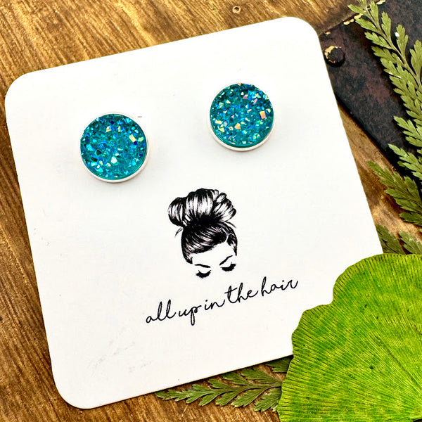 All Up In The Hair | Online Accessory Boutique Located in Mooresville, NC | Two Aquamarine Druzy set in a silver stud setting. The earrings are on a white, All Up In The Hair branded packaging card. The card is laying on a wood background, alongside green leaves.