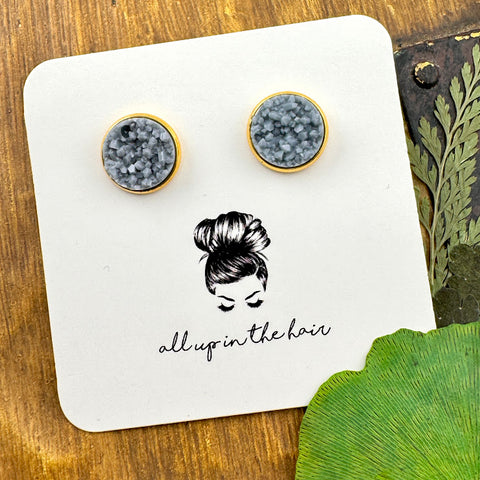 All Up In The Hair | Online Accessory Boutique Located in Mooresville, NC | Two ash grey druzies set in a gold earring setting. The earrings are on a white, All Up In The Hair branded packaging card. The card is laying on a wood background next to green leaves.