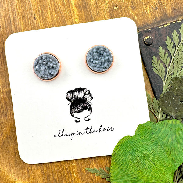 All Up In The Hair | Online Accessory Boutique Located in Mooresville, NC | Two ash grey druzies set in a rose gold earring setting. The earrings are on a white, All Up In The Hair branded packaging card. The card is laying on a wood background next to green leaves.