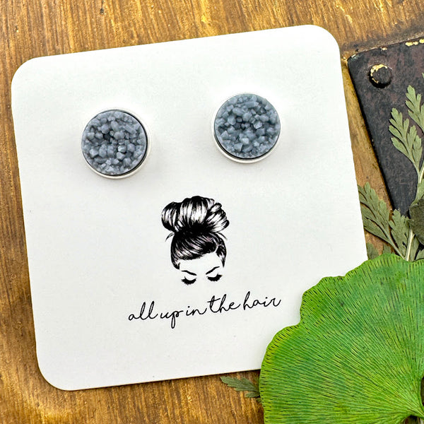 All Up In The Hair | Online Accessory Boutique Located in Mooresville, NC | Two ash grey druzies set in a silver earring setting. The earrings are on a white, All Up In The Hair branded packaging card. The card is laying on a wood background next to green leaves.