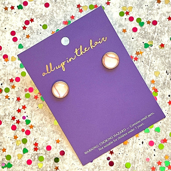All Up In The Hair | Online Accessory Boutique Located in Mooresville, NC | An indigo colored, All Up In The Hair branded packaging card laying on a grey background, surrounded by colorful glitter. On the card is two baseball studs.
