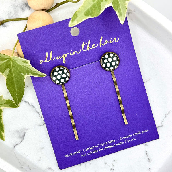 All Up In The Hair | Online Accessory Boutique Located in Mooresville, NC | Two Big Polka Dot Bobby Pins on an indigo colored, All Up In The Hair branded packaging card. The card is laying on a white marble background next to a wood bead garland and ivy leaves.