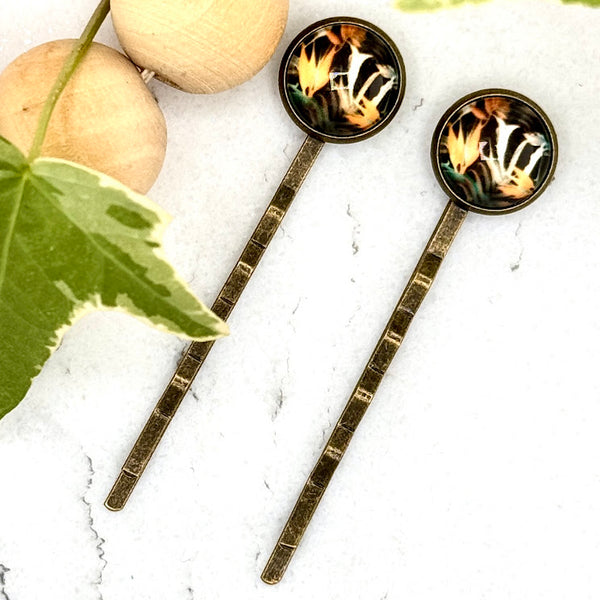 All Up In The Hair | Online Accessory Boutique Located in Mooresville, NC | Two Bird of Paradise Bobby Pins on a white marble background. There is a wood bead garland and ivy leaves next to the bobby pins.