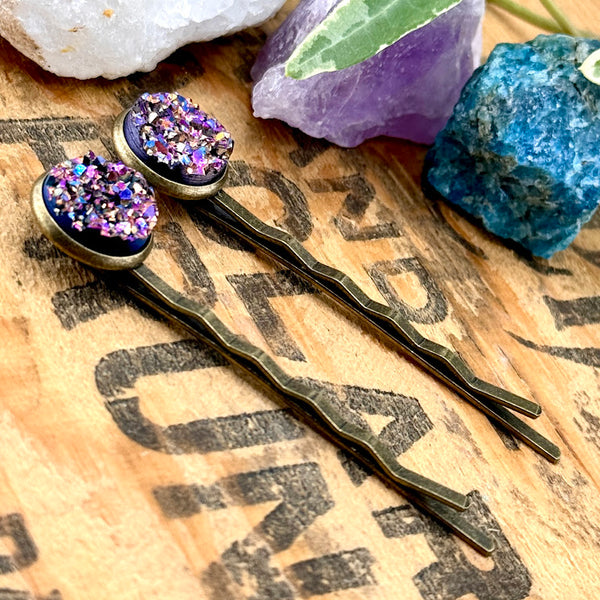 All Up In The Hair | Online Accessory Boutique Located in Mooresville, NC | Side view of two Bismuth Druzy Bobby Pins. There are crystals and ivy leaves at the top of the image.