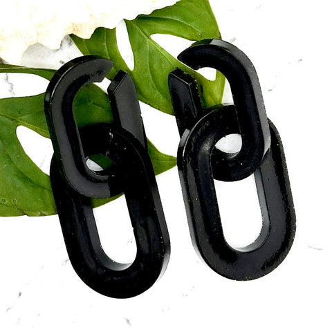 All Up In The Hair | Online Accessory Boutique Located in Mooresville, NC | Two Black Chunky Chain Earrings laying on two monstera leaves on a white marble background.