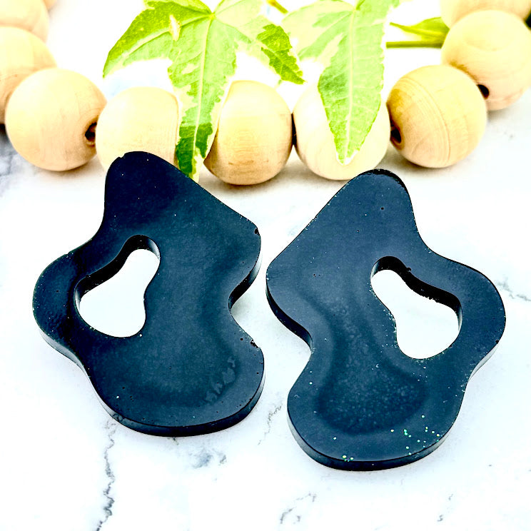 All Up In The Hair | Online Accessory Boutique Located in Mooresville, NC | Two Black Wave Earrings on a white marble background. Behind the earrings is a wood bead garland and ivy leaves.