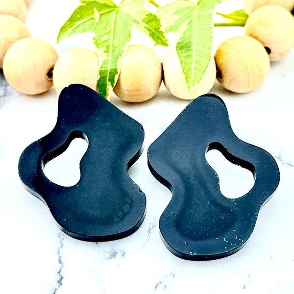 All Up In The Hair | Online Accessory Boutique Located in Mooresville, NC | Two Black Wave Earrings on a white marble background. Behind the earrings is a wood bead garland and ivy leaves.