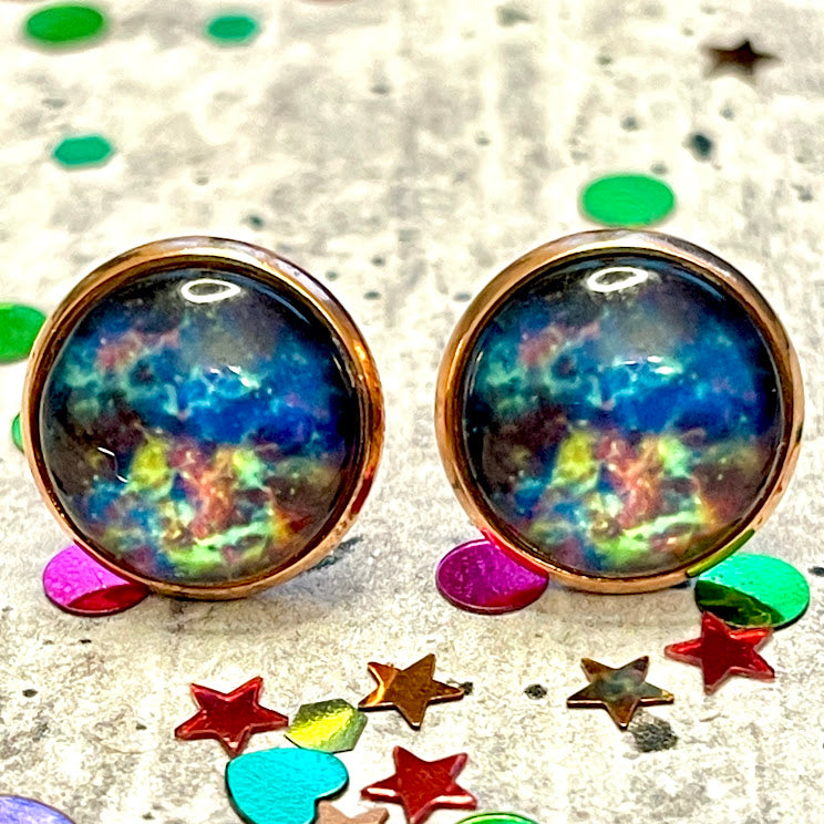 All Up In The Hair | Online Accessory Boutique Located in Mooresville, NC | Close up of two blue galaxy earrings laying on a gray background, surrounded by colorful glitter.
