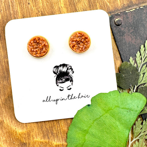 All Up In The Hair | Online Accessory Boutique Located in Mooresville, NC | Two camel druzies set in gold earring settings. The earrings are on a white, All Up In The Hair branded packaging card. The card is laying on a wood background next to green leaves.