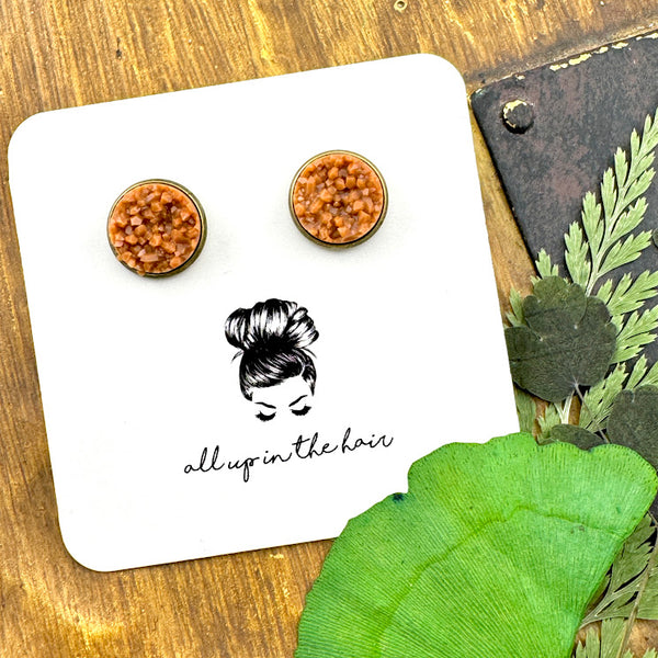 All Up In The Hair | Online Accessory Boutique Located in Mooresville, NC | Two camel druzies set in bronze earring settings. The earrings are on a white, All Up In The Hair branded packaging card. The card is laying on a wood background next to green leaves.