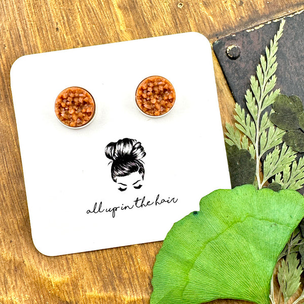 All Up In The Hair | Online Accessory Boutique Located in Mooresville, NC | Two camel druzies set in silver earring settings. The earrings are on a white, All Up In The Hair branded packaging card. The card is laying on a wood background next to green leaves.