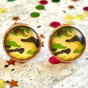 All Up In The Hair | Online Accessory Boutique Located in Mooresville, NC | Close up of two camo earrings laying on a gray background, surrounded by colorful glitter.
