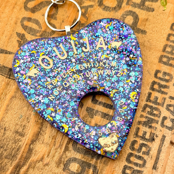 All Up In The Hair | Online Accessory Boutique Located in Mooresville, NC | Close up of our Celestial Planchette Keychain on a wood background with black lettering.