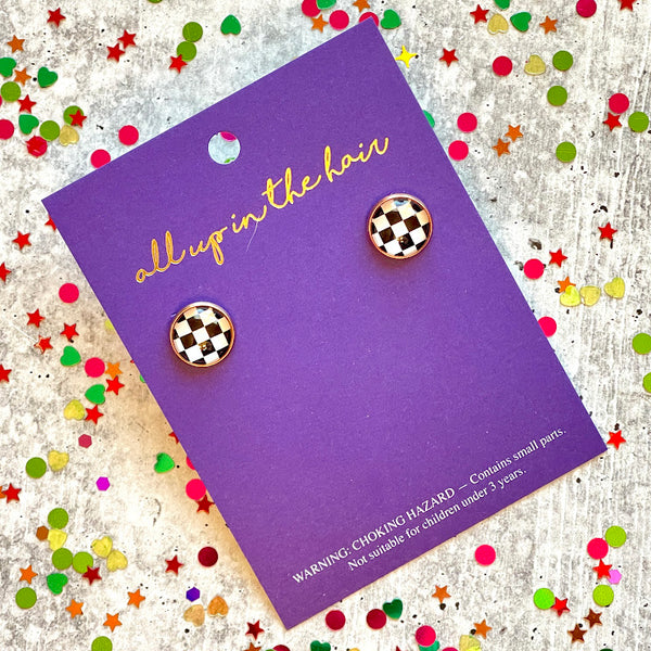 All Up In The Hair | Online Accessory Boutique Located in Mooresville, NC | An All Up In The Hair branded packaging card laying on a gray background, surrounded by colorful glitter. On the card is two checkered flag earrings.