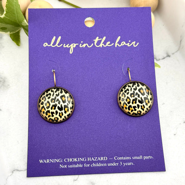 All Up In The Hair | Online Accessory Boutique Located in Mooresville, NC | Two Cheetah Dangle Earrings on an indigo colored, All Up In The Hair branded packaging card. The card is laying on a white marble background .