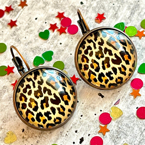 All Up In The Hair | Online Accessory Boutique Located in Mooresville, NC | Two cheetah print dangle earrings laying on a gray background surrounded by colorful glitter.