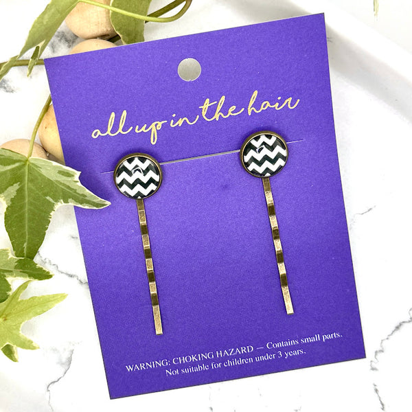 All Up In The Hair | Online Accessory Boutique Located in Mooresville, NC | Two Chevron Bobby Pins on an indigo colored, All Up In The Hair branded packaging card. The card is laying on a white marble background next to a wood bead garland and ivy leaves.