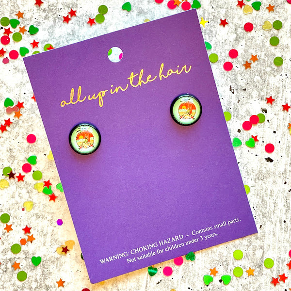 All Up In The Hair | Online Accessory Boutique Located in Mooresville, NC | An All Up In The Hair branded packaging card laying on a gray background, surrounded by colorful glitter. On the card is a pair of chillin' skeleton earrings.
