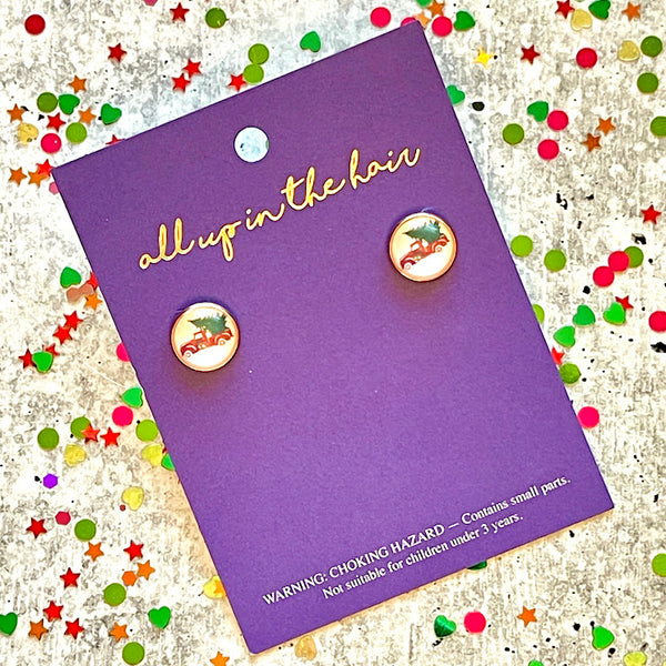 All Up In The Hair | Online Accessory Boutique Located in Mooresville, NC | An All Up In The Hair branded packaging card laying on a gray background, surrounded by colorful glitter. On the card is two christmas tree truck earrings.