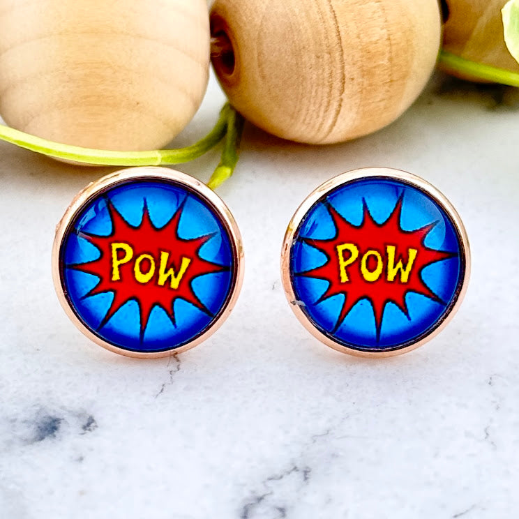 All Up In The Hair | Online Accessory Boutique Located in Mooresville, NC | Two Comic Pow Earrings on a white marble background. Behind the earrings is a wood bead garland and ivy leaves.