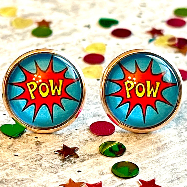 All Up In The Hair | Online Accessory Boutique Located in Mooresville, NC | Close up of two comic pow earrings laying on a gray background, surrounded by colorful glitter.