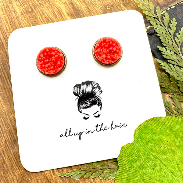 All Up In The Hair | Online Accessory Boutique Located in Mooresville, NC | Two Coral Druzy set in a bronze stud setting. The earrings are on a white, All Up In The Hair branded packaging card. The card is laying on a wood background alongside green leaves.
