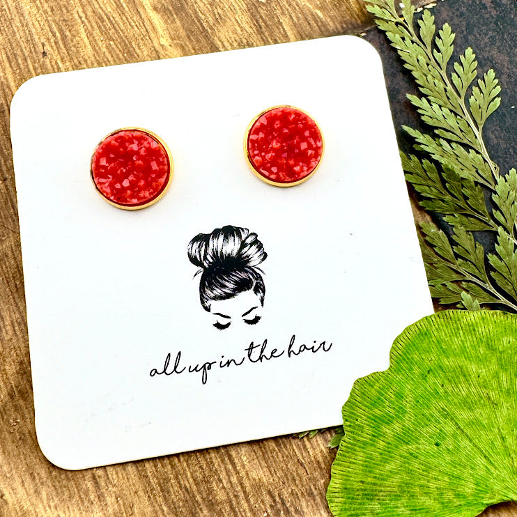 All Up In The Hair | Online Accessory Boutique Located in Mooresville, NC | Two Coral Druzy set in a gold stud setting. The earrings are on a white, All Up In The Hair branded packaging card. The card is laying on a wood background alongside green leaves.
