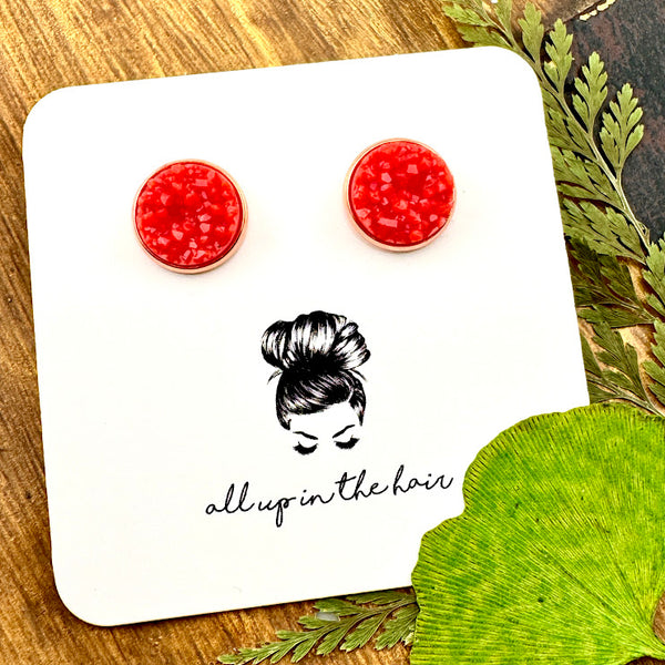 All Up In The Hair | Online Accessory Boutique Located in Mooresville, NC | Two Coral Druzy set in a rose gold stud setting. The earrings are on a white, All Up In The Hair branded packaging card. The card is laying on a wood background alongside green leaves.
