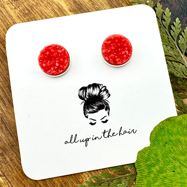 All Up In The Hair | Online Accessory Boutique Located in Mooresville, NC | Two Coral Druzy set in a silver stud setting. The earrings are on a white, All Up In The Hair branded packaging card. The card is laying on a wood background alongside green leaves.
