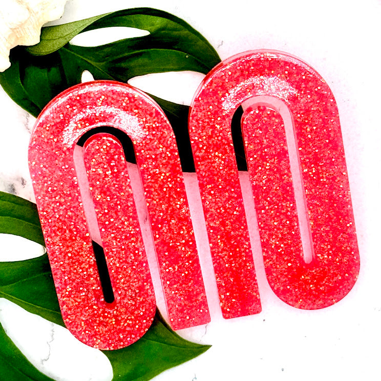 All Up In The Hair | Online Accessory Boutique Located in Mooresville, NC | Two coral paperclip earrings laying on a white background. Behind the earrings is some monstera leaves and a shell.