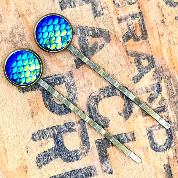 All Up In The Hair | Online Accessory Boutique Located in Mooresville, NC | Two Dark Blue Mermaid Bobby Pins laying on a wood background with black lettering.
