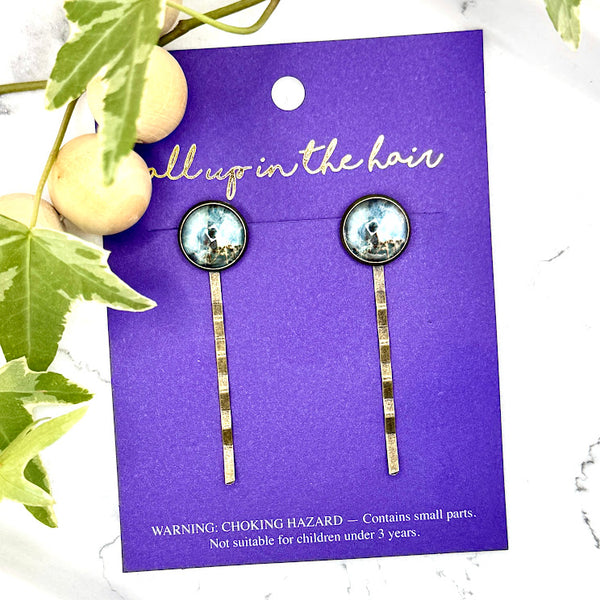All Up In The Hair | Online Accessory Boutique Located in Mooresville, NC | Two Dark Marble Bobby Pins on an indigo colored, All Up In The Hair branded packaging card. The card is laying on a white marble background, next to a wood bead garland and ivy leaves.