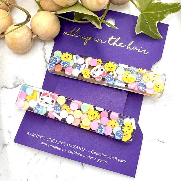 All Up In The Hair | Online Accessory Boutique Located in Mooresville, NC | Our Easter Basket Barrette Set on an indigo colored, All Up In The Hair branded packaging card. The card is laying on a white marble background. At the top of the image is a wood bead garland and ivy leaves.