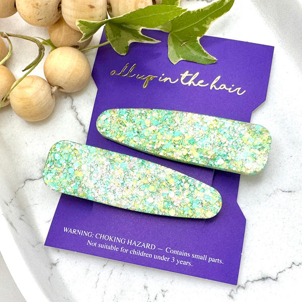 All Up In The Hair | Online Accessory Boutique Located in Mooresville, NC | Our Easter Basket Barrette Set on an indigo colored, All Up In The Hair branded packaging card. The card is laying on a white marble background. At the top of the image is a wood bead garland and ivy leaves. 