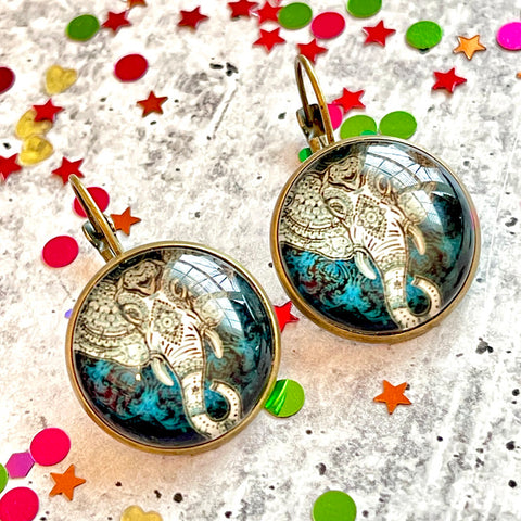 All Up In The Hair | Online Accessory Boutique Located in Mooresville, NC | Two Mandala Elephant Dangle Earrings laying on a gray background, surrounded by colorful glitter.