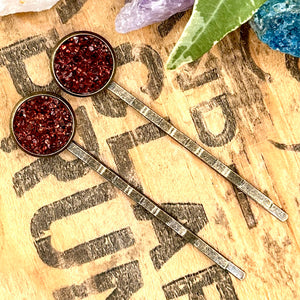 All Up In The Hair | Online Accessory Boutique Located in Mooresville, NC | Two brown bobby pins with orange undertones on a wood background with black lettering. There are crystals and ivy leaves at the top of the image.
