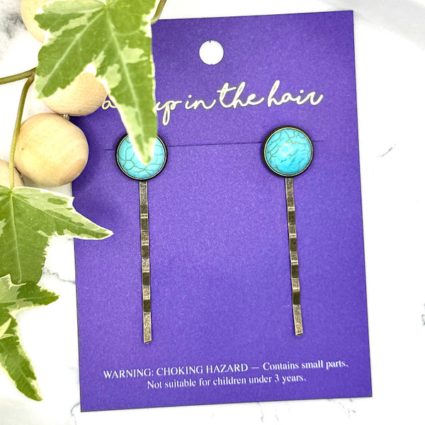 All Up In The Hair | Online Accessory Boutique Located in Mooresville, NC | Two Faux Turquoise Bobby Pins on an All Up In The Hair branded packaging card. The card is laying on a gray background, surrounded by colorful glitter.