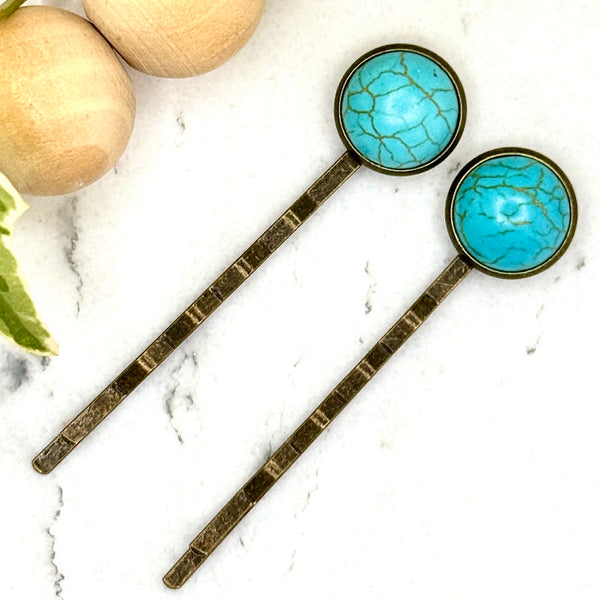 All Up In The Hair | Online Accessory Boutique Located in Mooresville, NC | Two Faux Turquoise Bobby Pins laying on a white marble background next to a wood bead garland and ivy leaves.