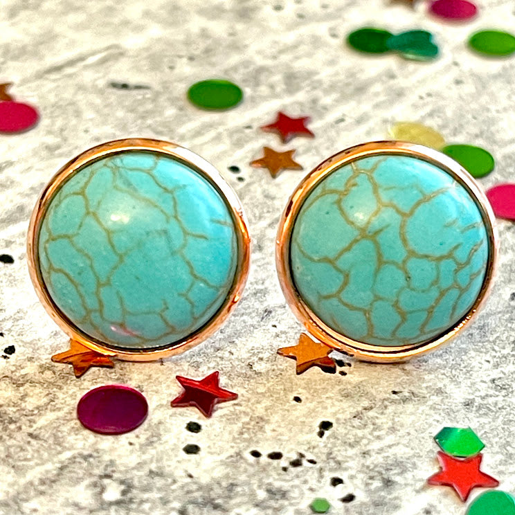 All Up In The Hair | Online Accessory Boutique Located in Mooresville, NC | Two faux turquoise stud earrings laying on a gray background, surrounded by colorful glitter.