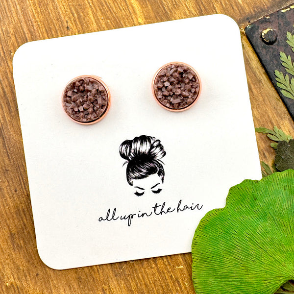 All Up In The Hair | Online Accessory Boutique Located in Mooresville, NC | Two fawn brown druzies set in a rose gold earrings setting. The earrings are on a white, All Up In The Hair branded packaging card. The card is laying on a wood background alongside green leaves.