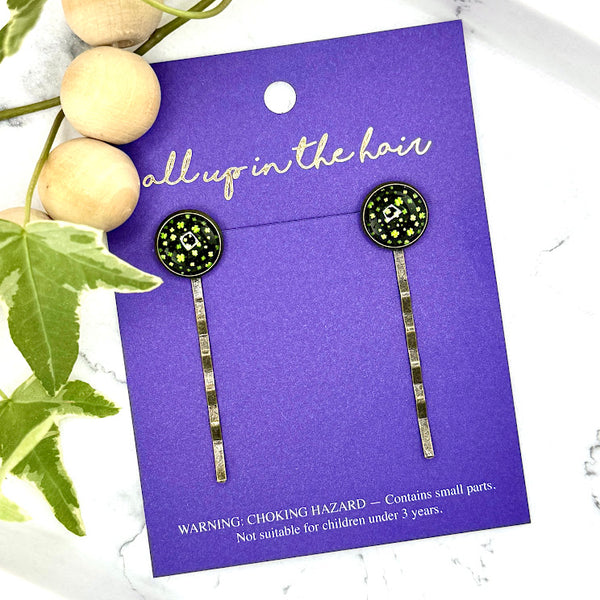 All Up In The Hair | Online Accessory Boutique Located in Mooresville, NC | Two Field Of Clover Bobby Pins on an indigo colored, All Up In The Hair branded packaging card. The card is laying on a white marble background, next to a wood bead garland and ivy leaves.