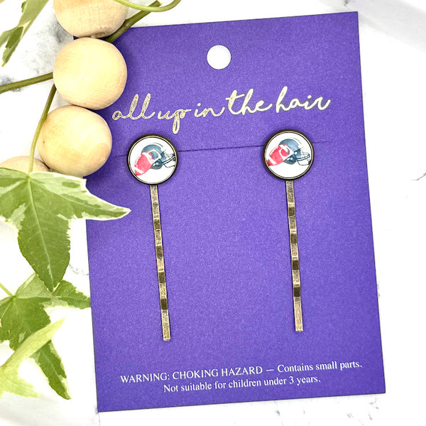 All Up In The Hair | Online Accessory Boutique Located in Mooresville, NC | Two Football Bobby Pins on an indigo colored, All Up In The Hair branded packaging card. The card is laying on a white marble background next to a wood bead garland and ivy leaves.
